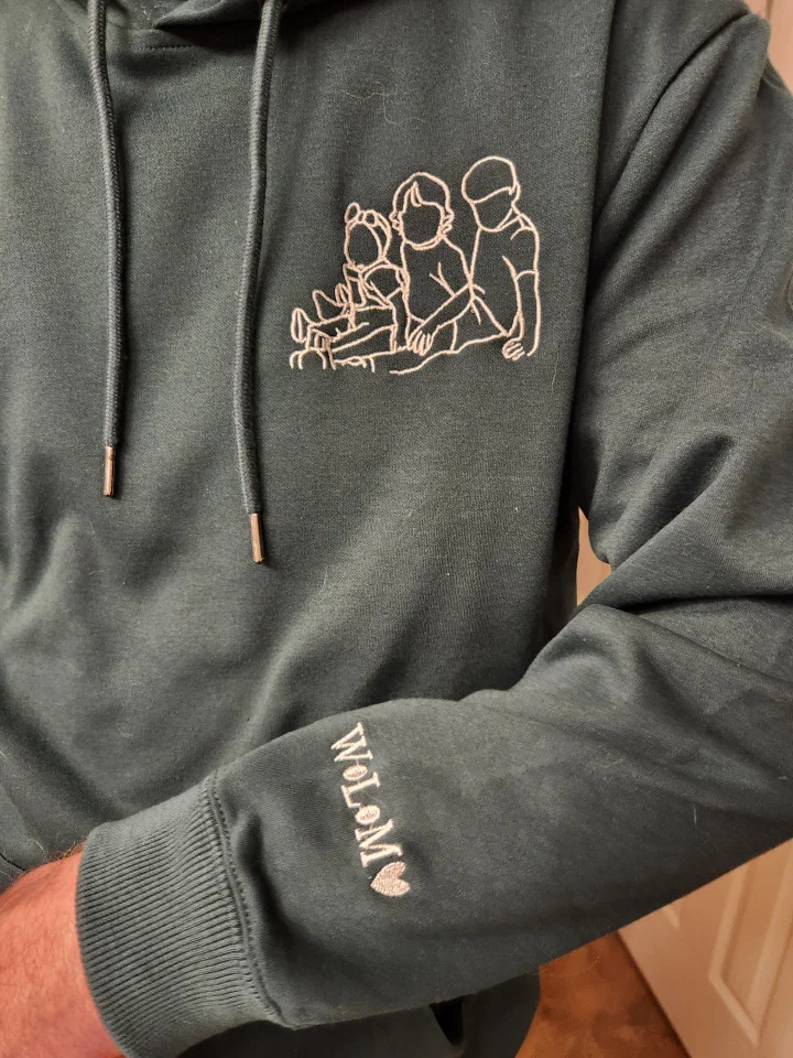Kundin zeigt grünen bestickten Pullover mit ihrem Hund und Namen am Ärmel